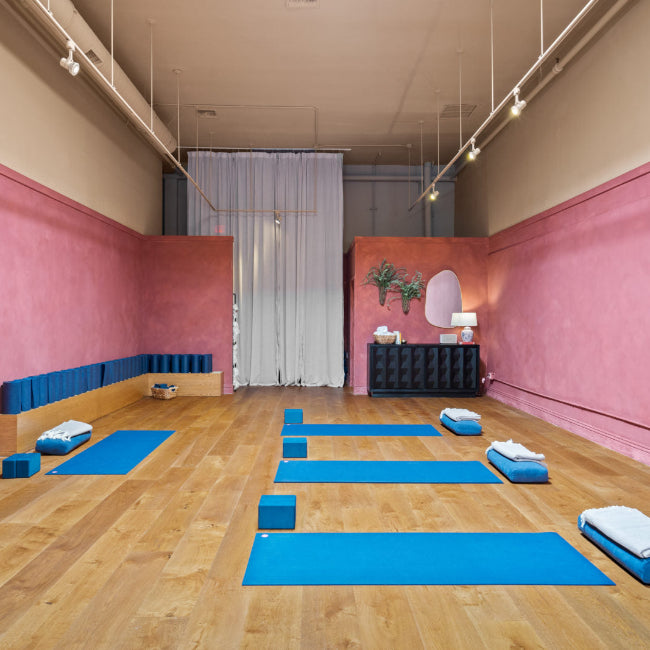 Pilates studio with blue mats on wooden floor and pink walls