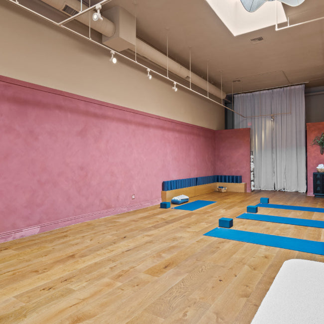 Yoga studio with pink walls, wooden floor, and blue yoga mats.